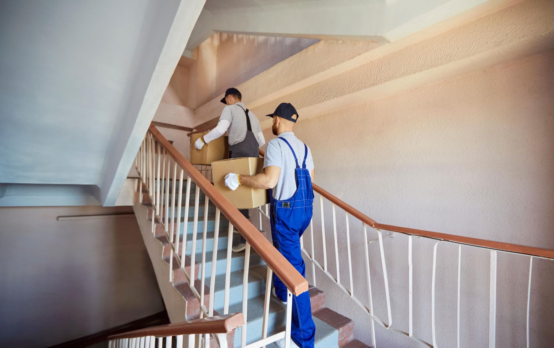 Two workers carrying boxes up a curved indoor staircase with white railings