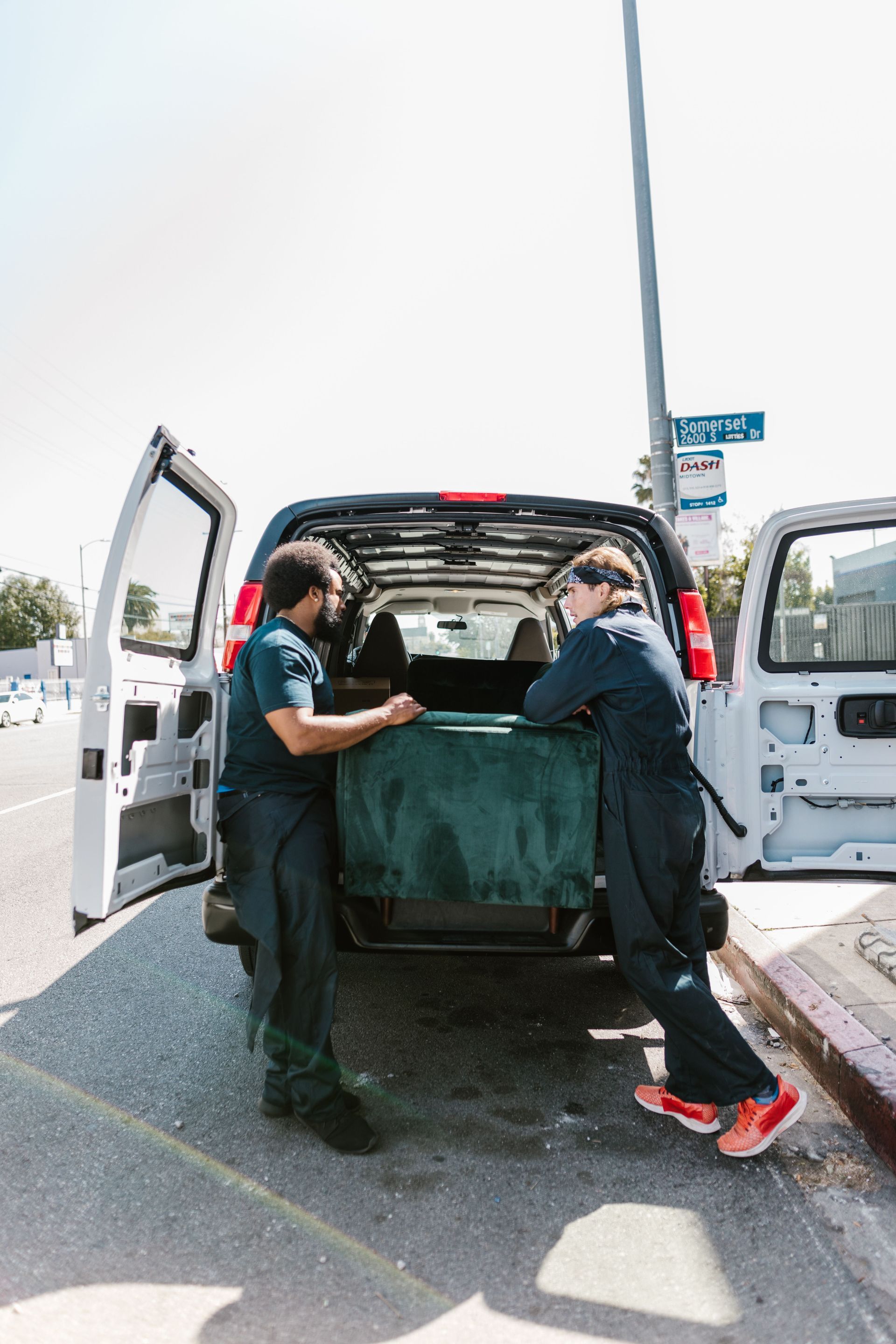 Two workers loading a large item into a white van at the roadside.
