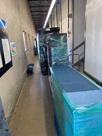 Narrow hallway with wrapped equipment and boxes stacked along the wall, creating a tight passage.
