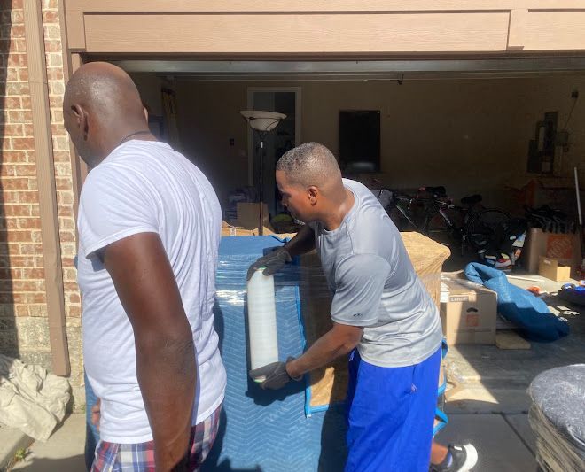 Two people move a large blue appliance into a garage full of items.