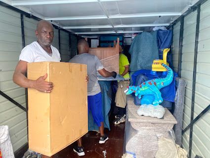 Men loading boxed and wrapped items into a moving truck, with a blue toy on top.