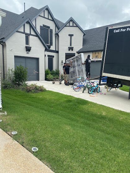 Moving truck and furniture on a driveway outside a white house with a green lawn