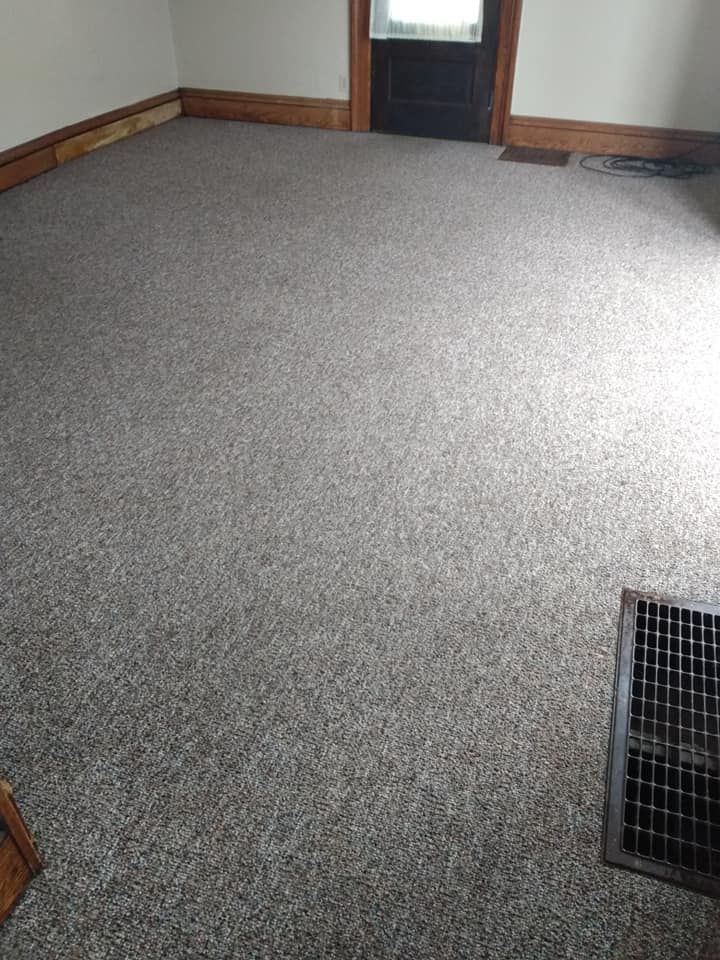 Empty carpeted room with a dark door, wood trim, and floor vent.