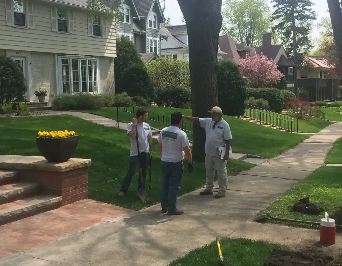 Three men are standing on a sidewalk in front of a house