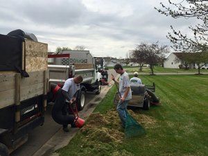 A group of men are working on a lawn in front of a dump truck.