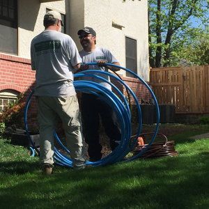 Two men are standing in front of a house holding a bunch of blue pipes.