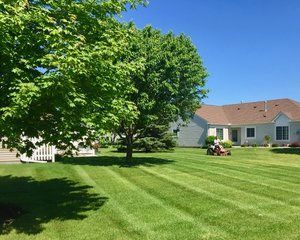 A person is mowing a lush green lawn in front of a house.