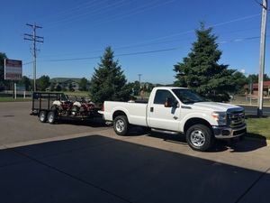 A white truck is towing a trailer with atvs on it.