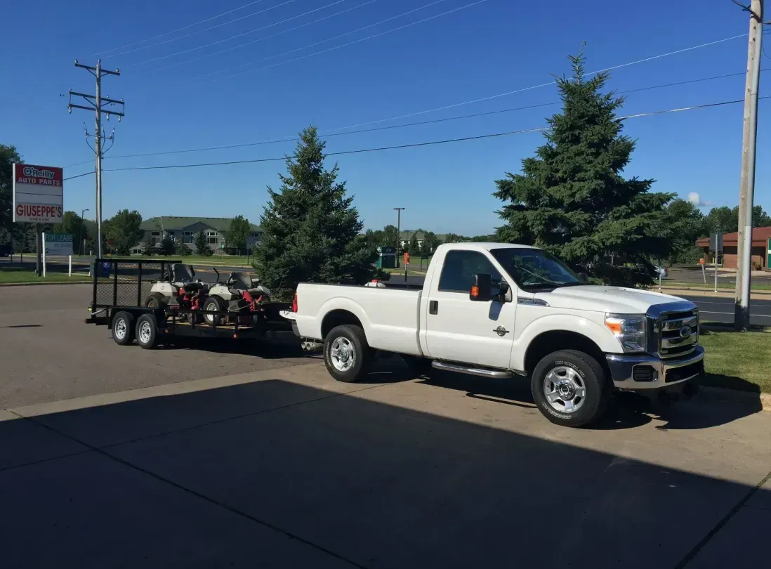 A white truck with a trailer attached to it is parked in a parking lot.