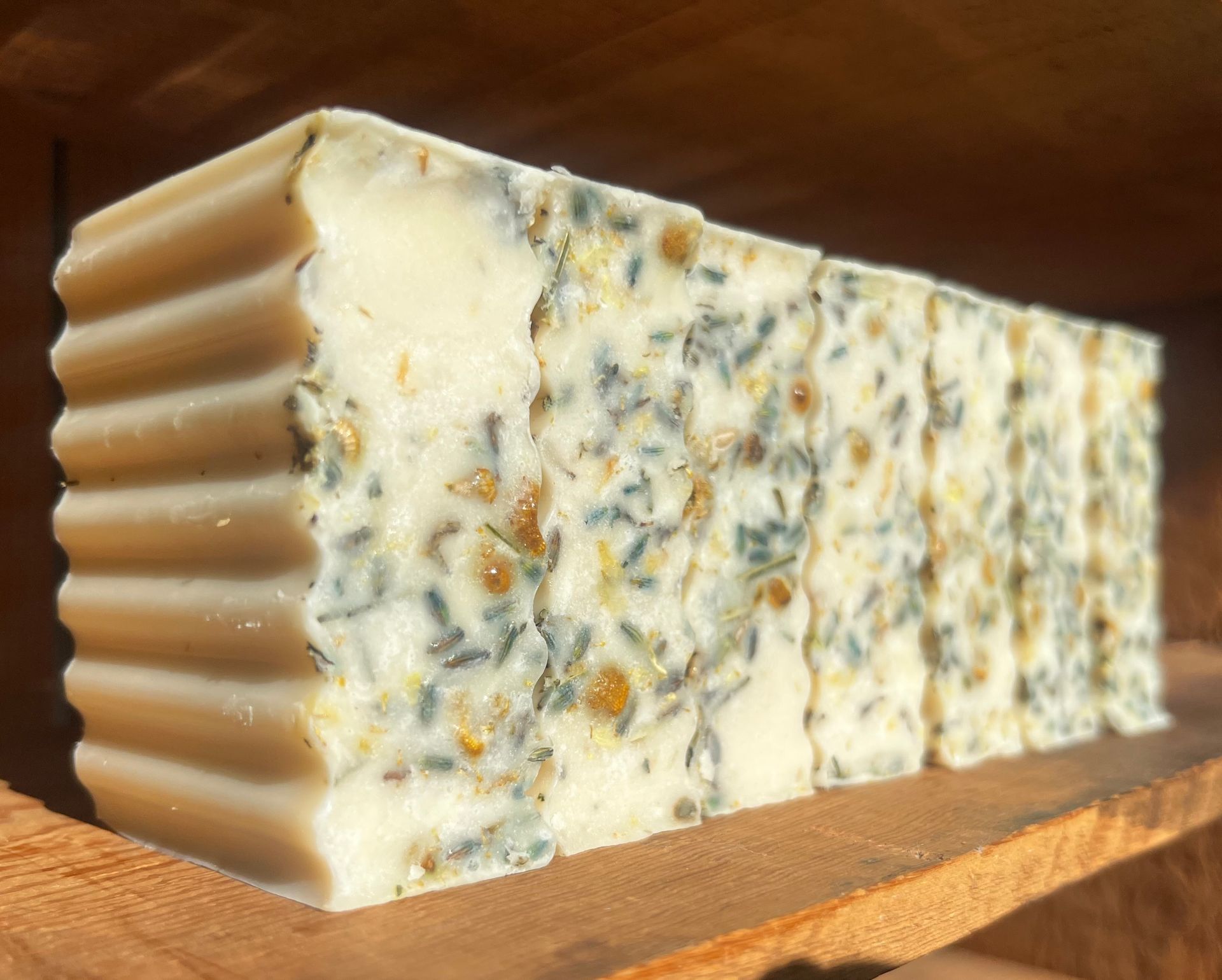 Bar of speckled handmade soap with a ridged tan side, resting on a wooden surface.