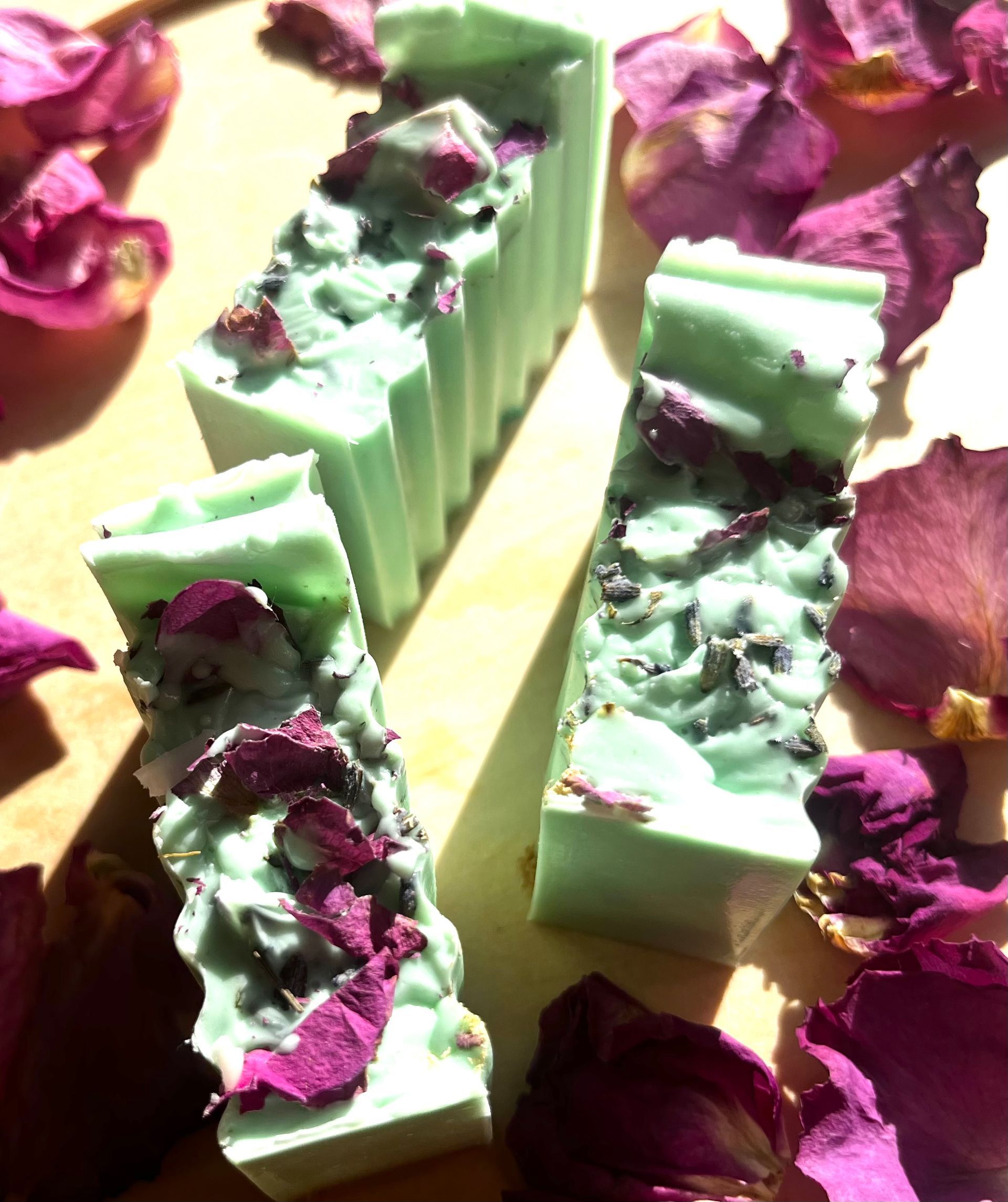 Mint green soap bars topped with dark purple flower petals on a light background