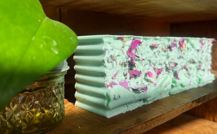 Mint-green and pink decorative soap bars on a wooden tray beside a leaf-shaped glass dish