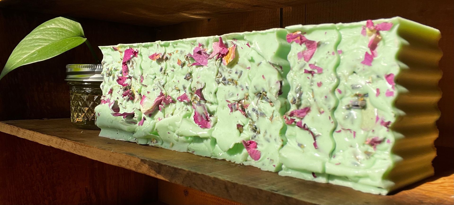 Mint green soap bars topped with dark purple flower petals on a light background