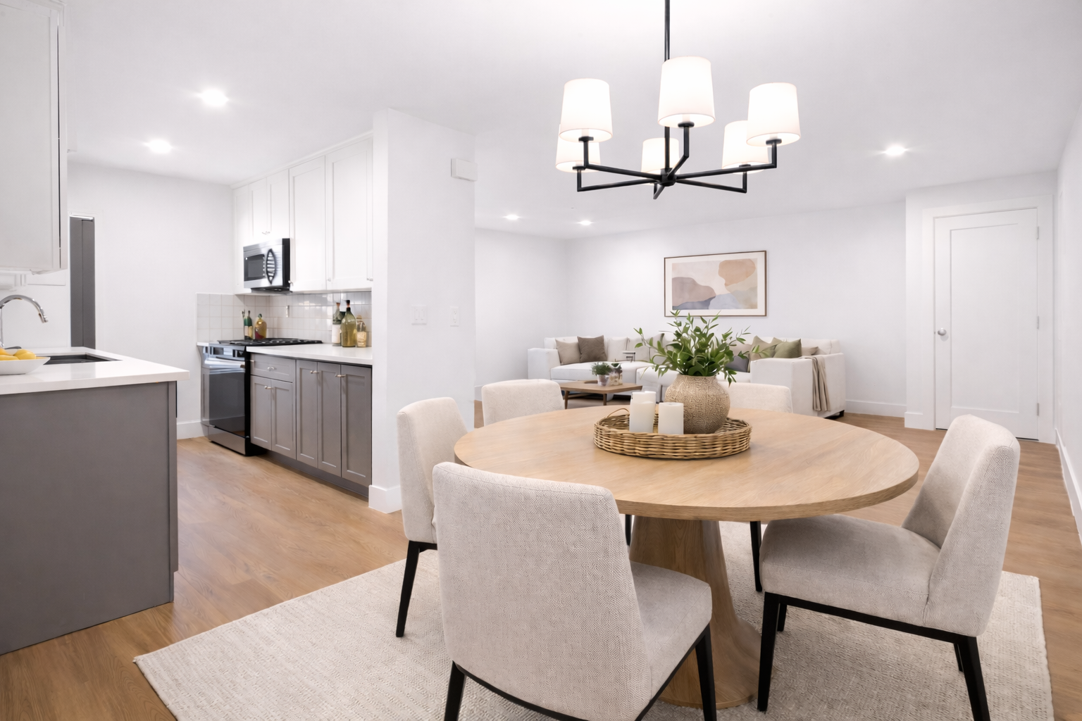 Open kitchen and dining area with round wooden table, beige chairs, and modern chandelier