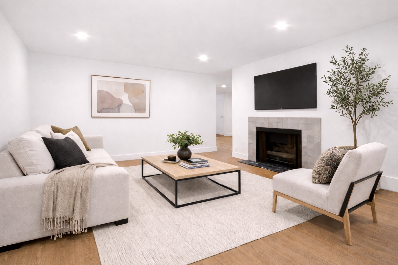 Bright modern living room with beige sofas, coffee table, fireplace, wall TV, and a potted tree.