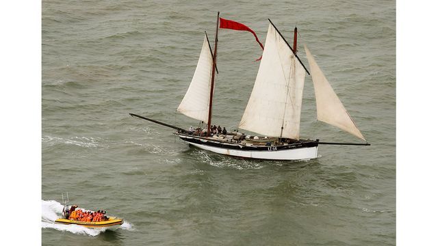 A boat with a red flag is going by a sailboat in the water