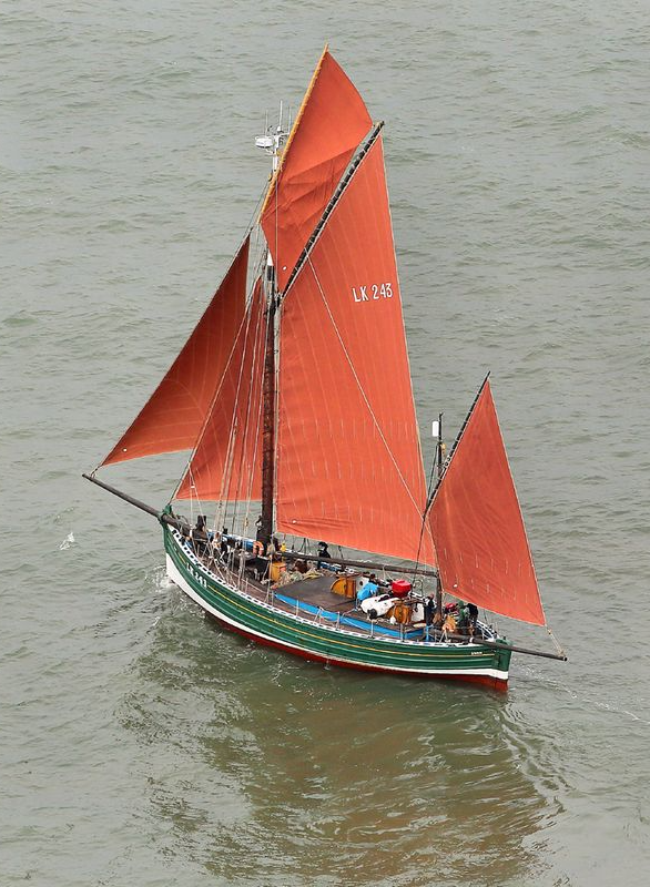 A green boat with red sails is floating on the water