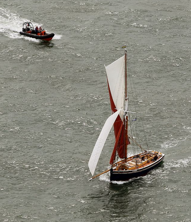 A boat with a red sail is floating in the water next to another boat