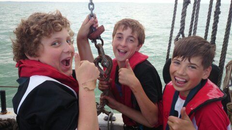 Three young lads grin and give a thumbs up while learning the ropes onboard