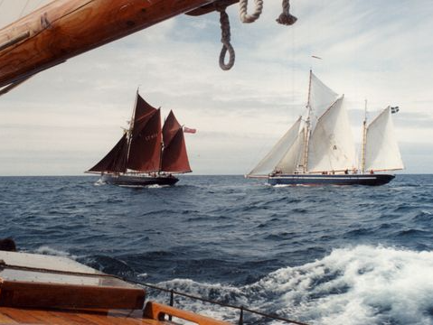 Two sailboats are in the ocean and one has a flag on the mast
