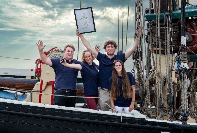 Skipper, crew and young people celebrating their achievement holding aloft a certificate onboard the boat