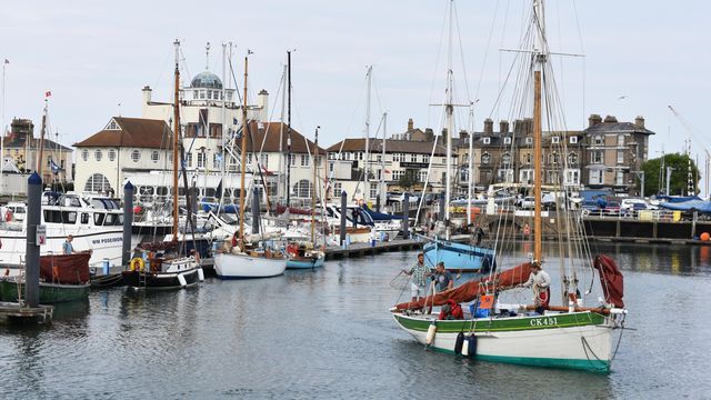 A group of boats are docked in a harbor with buildings in the background.