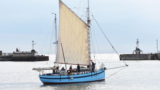A blue sailboat is floating on top of a body of water.