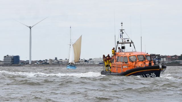 A lifeboat is floating on top of a body of water next to a sailboat.