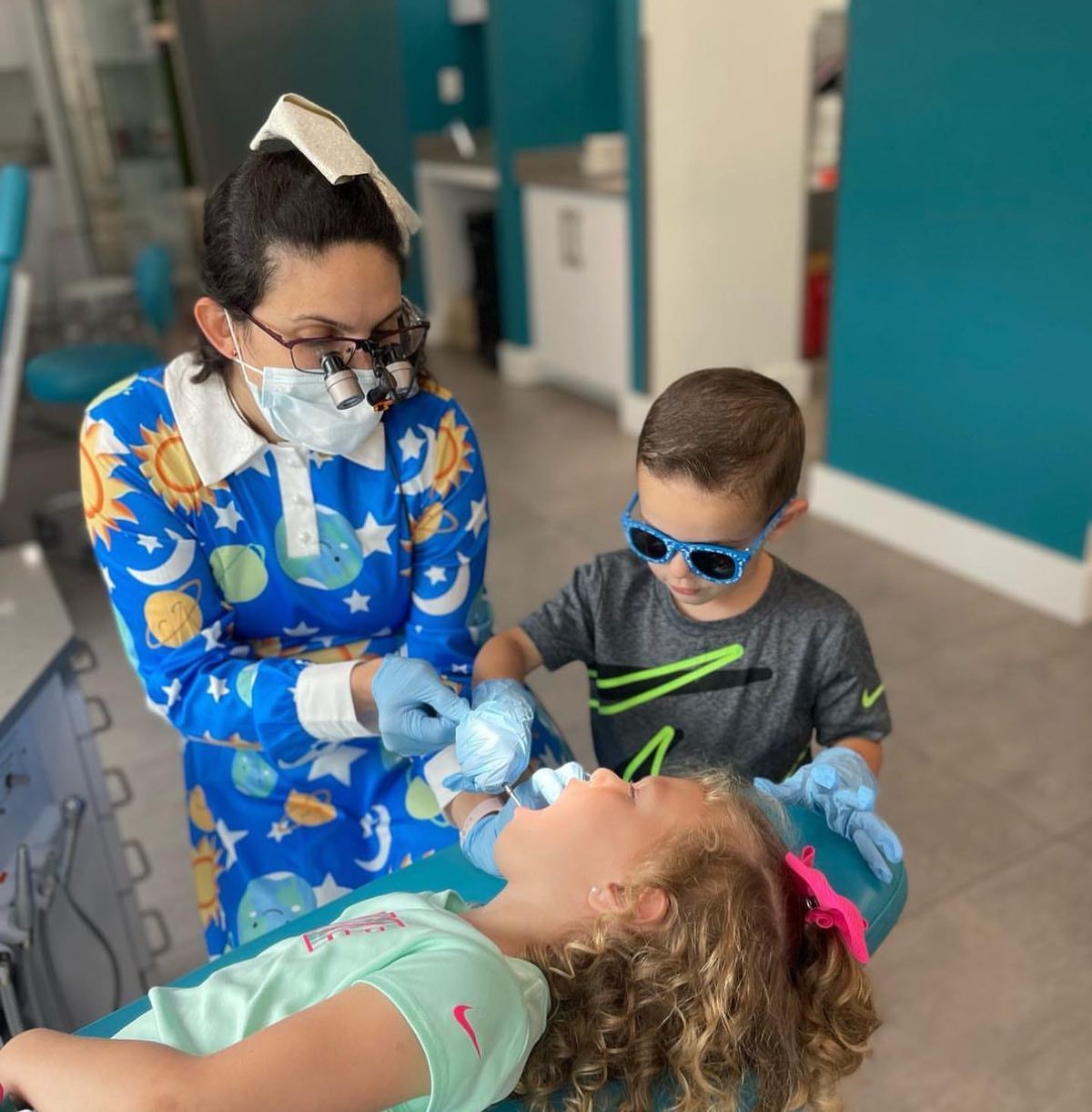 Dentist examining a child with tools while another child watches in a clinic room