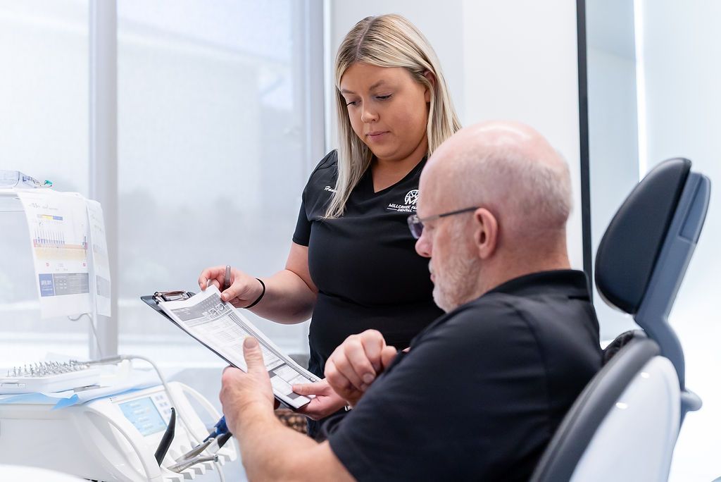 Clinic worker showing documents to a seated patient in a bright medical office.
