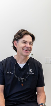 Man in black scrubs smiling while seated against a plain white wall