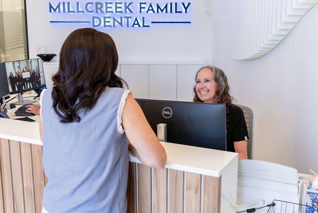 Dental reception desk with a smiling receptionist assisting a visitor at Millcreek Family Dental.