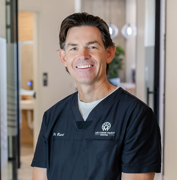 Smiling clinician in navy scrubs standing in a bright hospital hallway