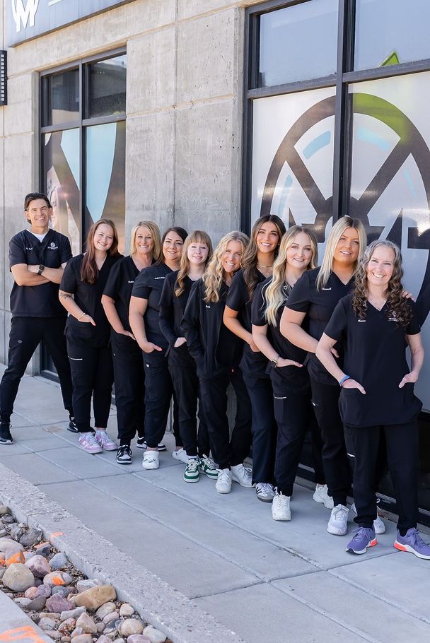 Group of people in black uniforms posing outside a building with large windows and wheel graphics.