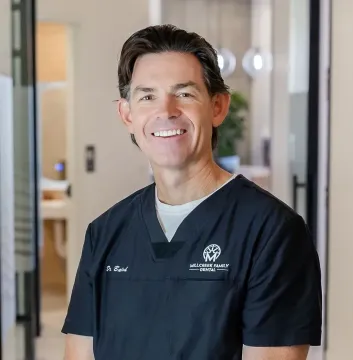 Smiling clinician in navy scrubs standing in a bright hospital hallway