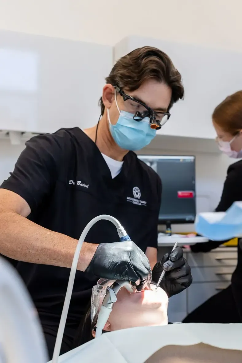 Dentist wearing a mask and gloves treats a patient's teeth in a bright clinic