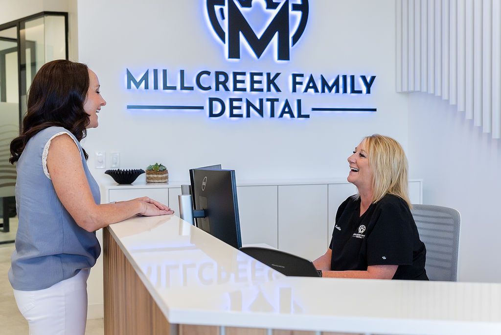 Dental office reception desk with two women talking under a Millcreek Family Dental sign