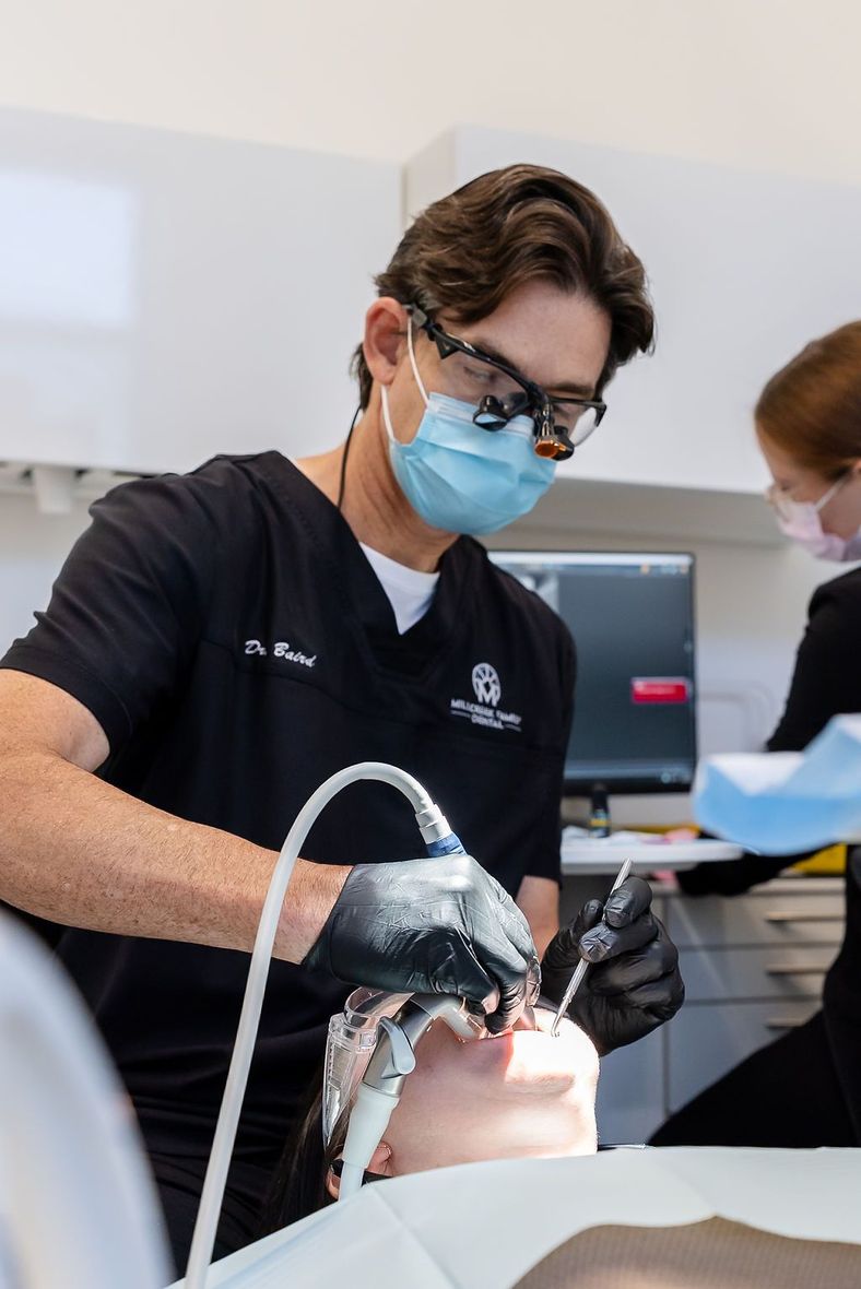 Dentist wearing a mask and gloves treats a patient's teeth in a bright clinic