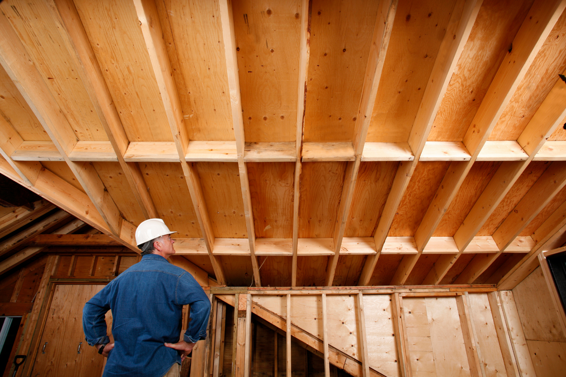 Man in hard hat inspecting exposed wooden ceiling joists.