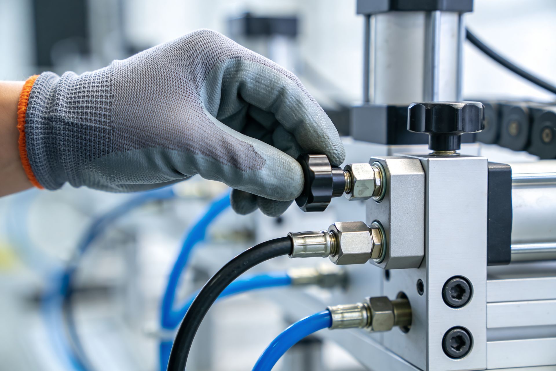 A gloved hand adjusts a knob on industrial pneumatic equipment with blue hoses.