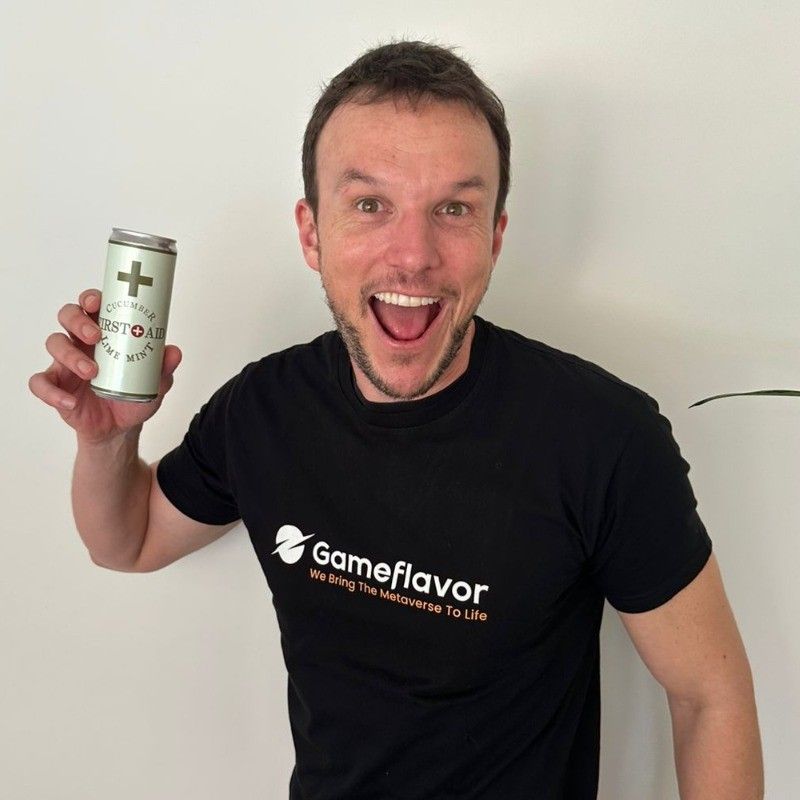 Man holding a Gameflavor energy drink, smiling with wide eyes. He's wearing a black Gameflavor t-shirt. White background.
