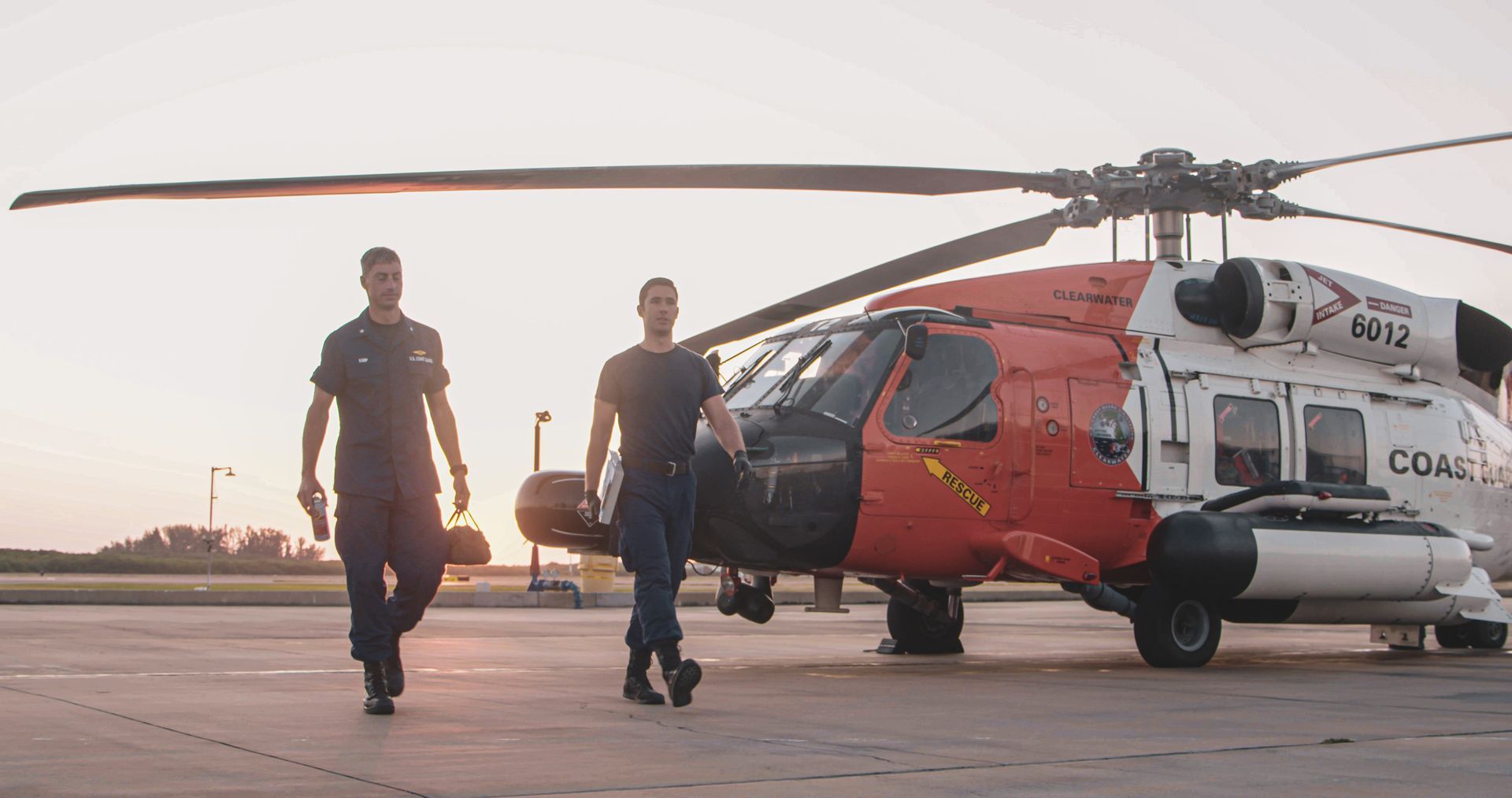 Two men are walking towards a helicopter on a runway.