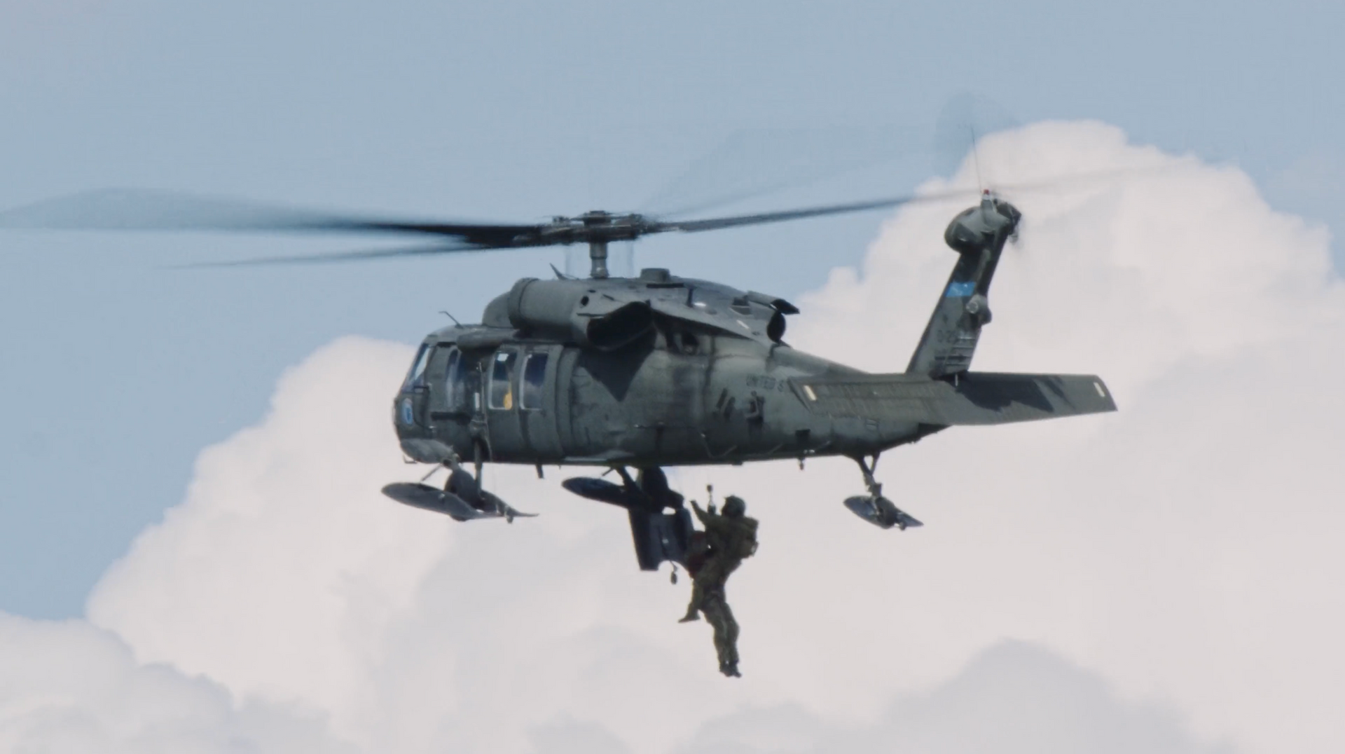 A helicopter is flying in the sky with a man hanging from it