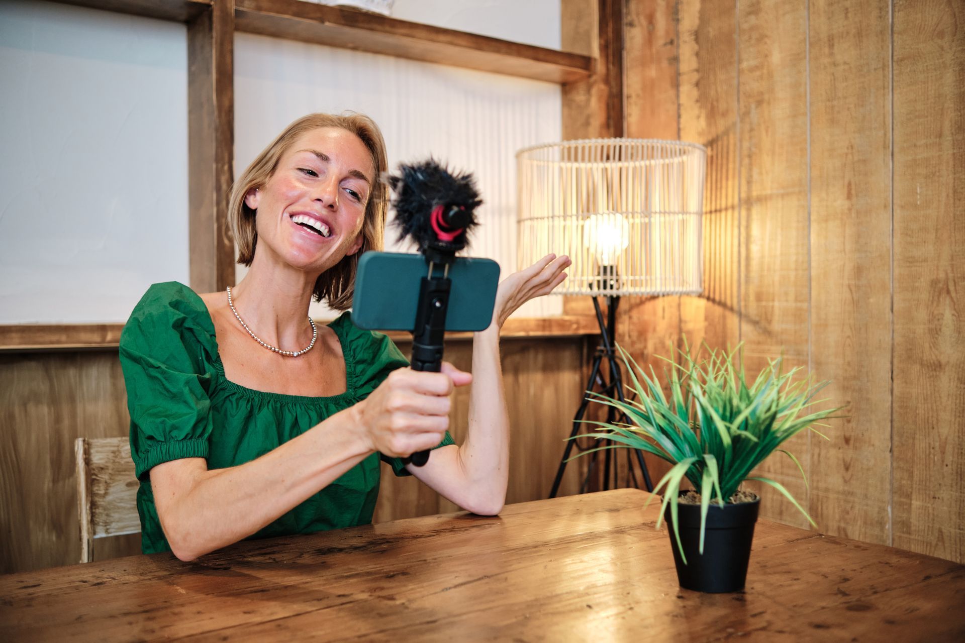 A woman is sitting at a table holding a microphone and a cell phone.