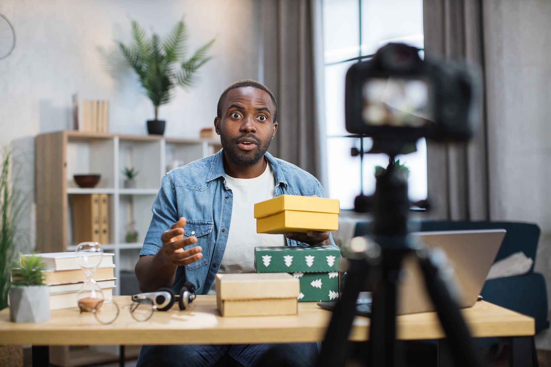 A man is sitting at a desk holding a box in front of a camera.