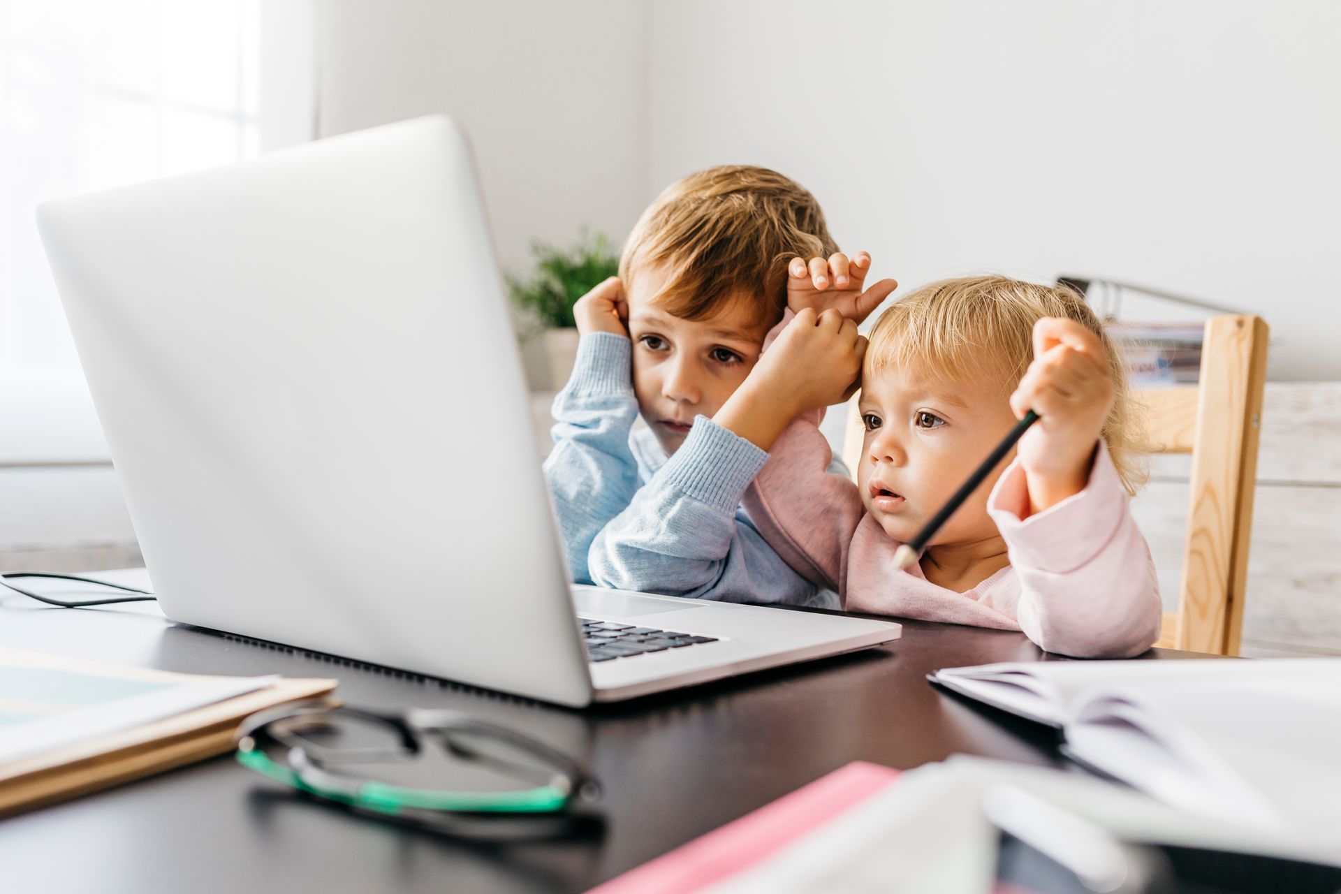 Two children are sitting at a table looking at a laptop computer.
