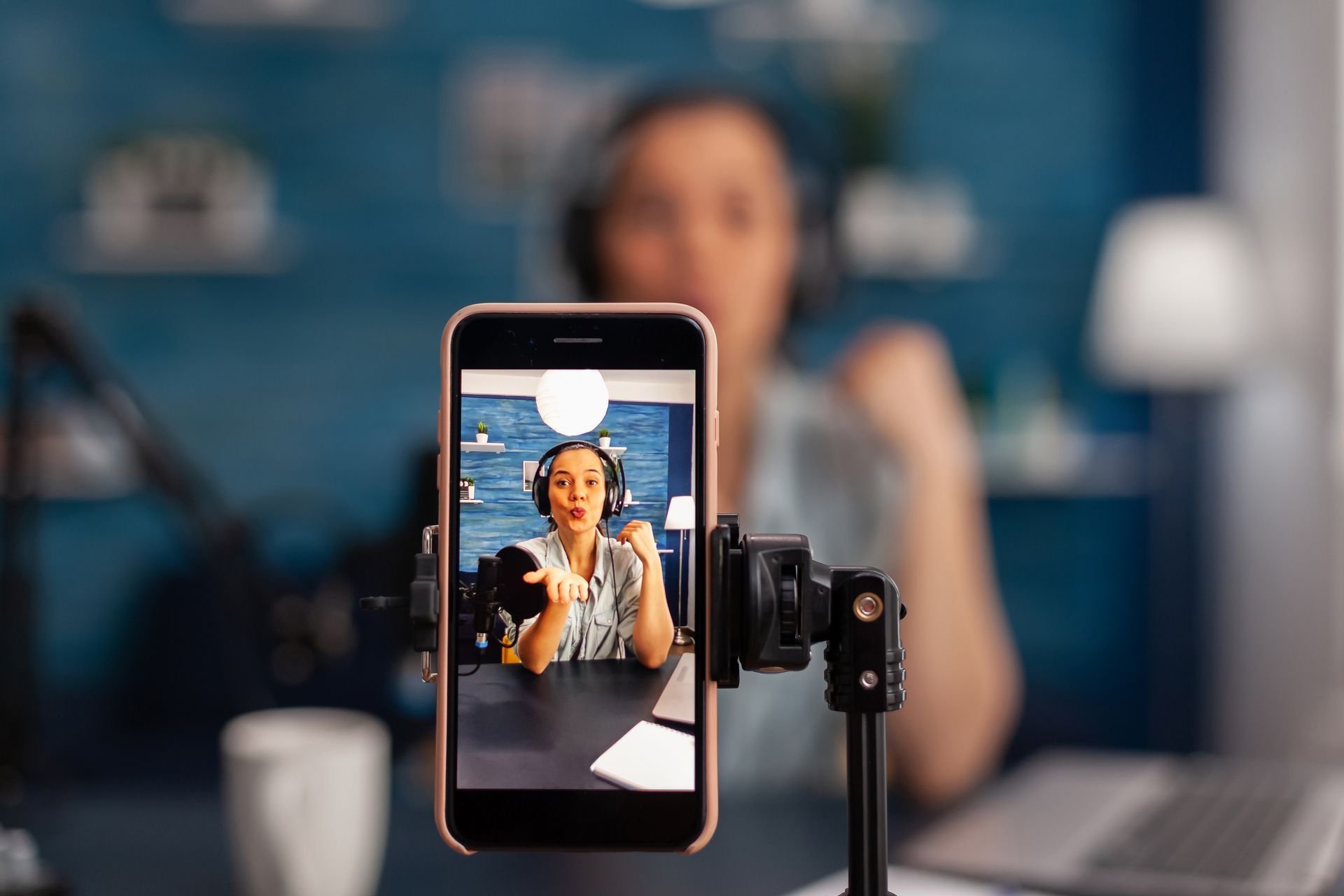 A woman wearing headphones is recording a video on a cell phone.