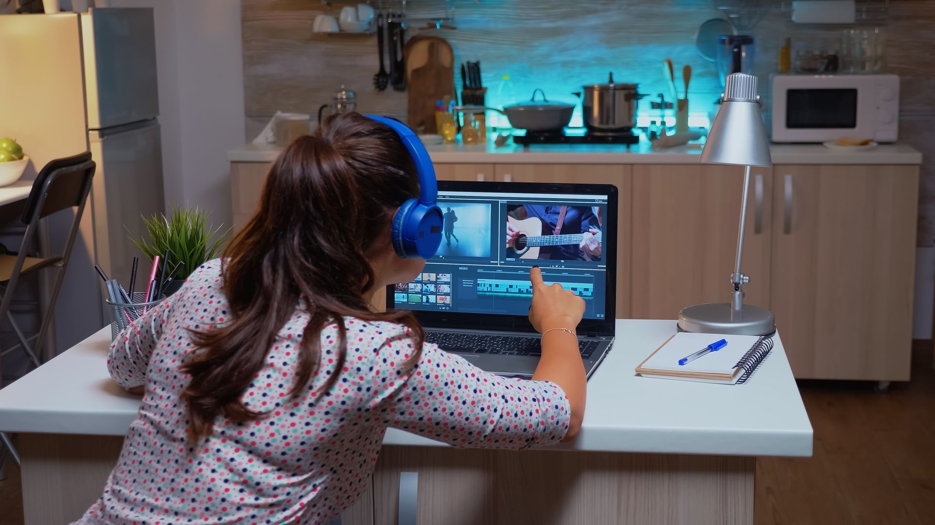A woman wearing headphones is using a laptop computer in a kitchen.