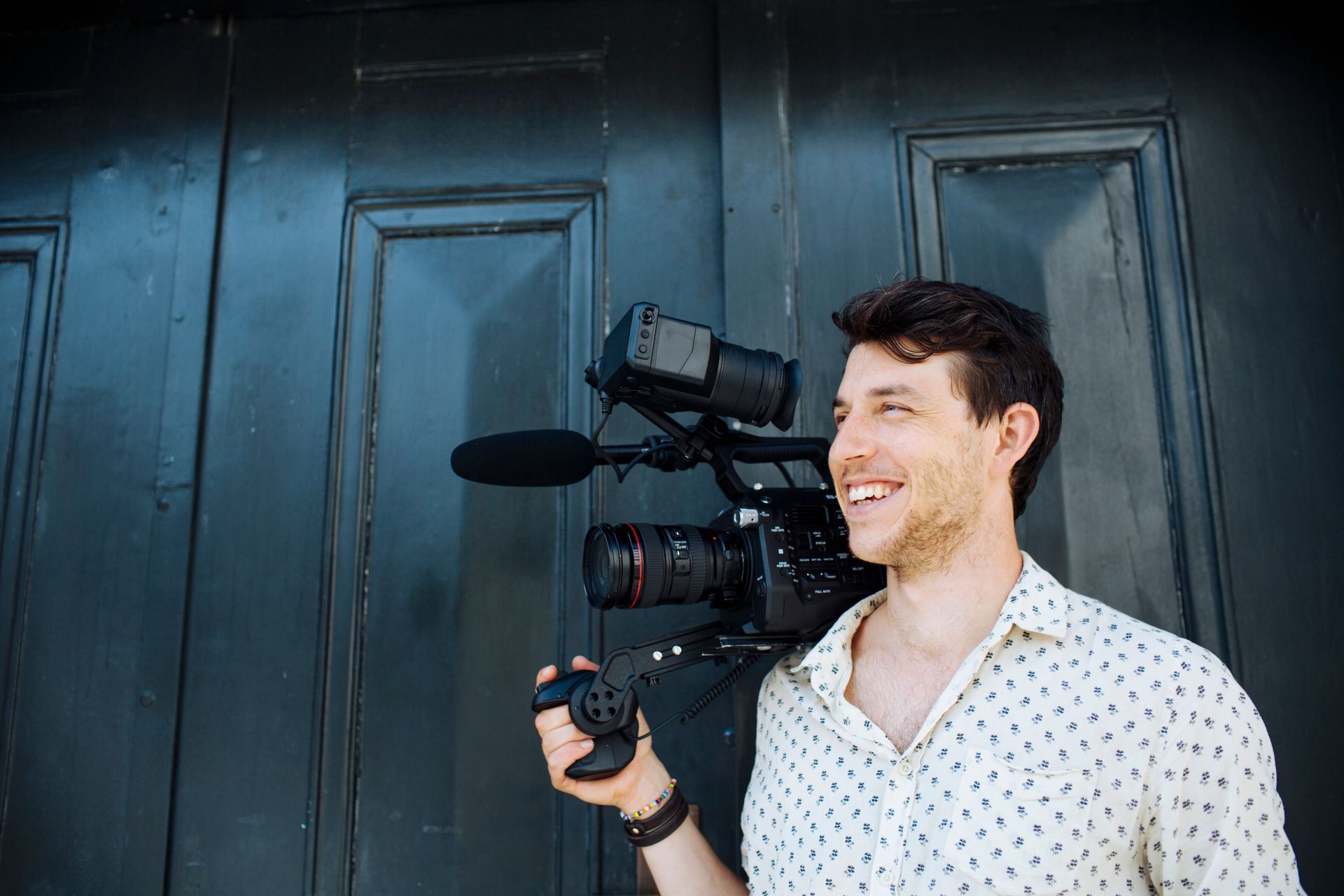 A man is holding a video camera in front of a black door.