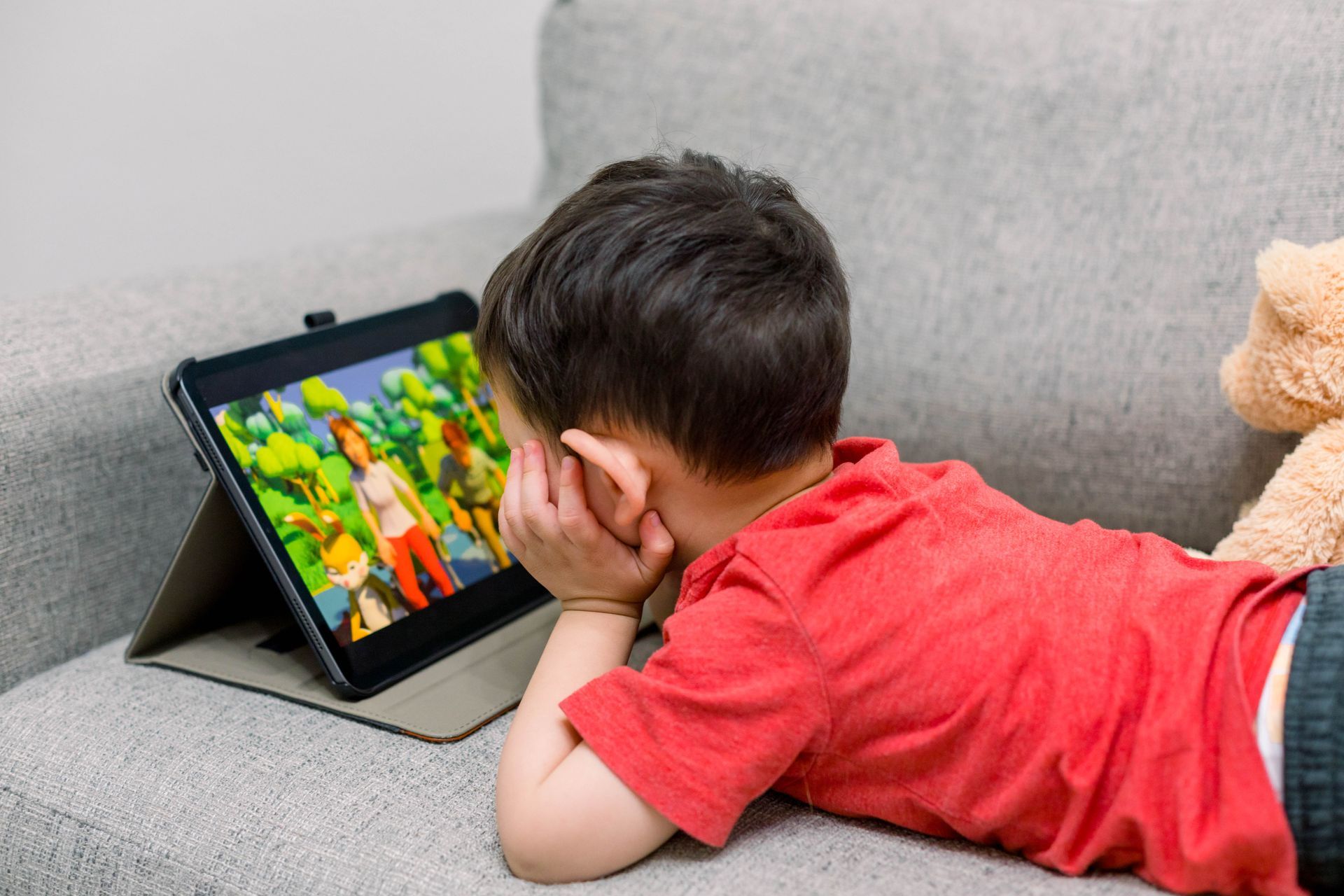 A young boy is laying on a couch looking at a tablet.